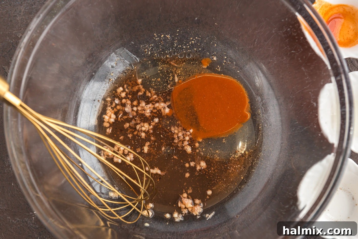 Prairie Jewel Dip 5 Step-by-step image showing whisking together the dressing ingredients: hot sauce, oil, red wine vinegar, and minced garlic in a large mixing bowl.