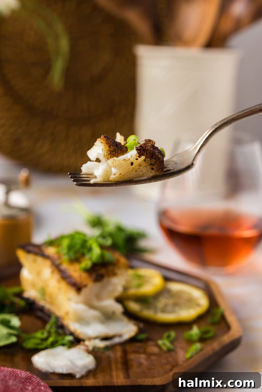 Golden Pan-Seared Chilean Sea Bass 11 Piece of Pan Seared Chilean Sea Bass on a fork held above a plate of Pan Seared Chilean Sea Bass, ready to eat.