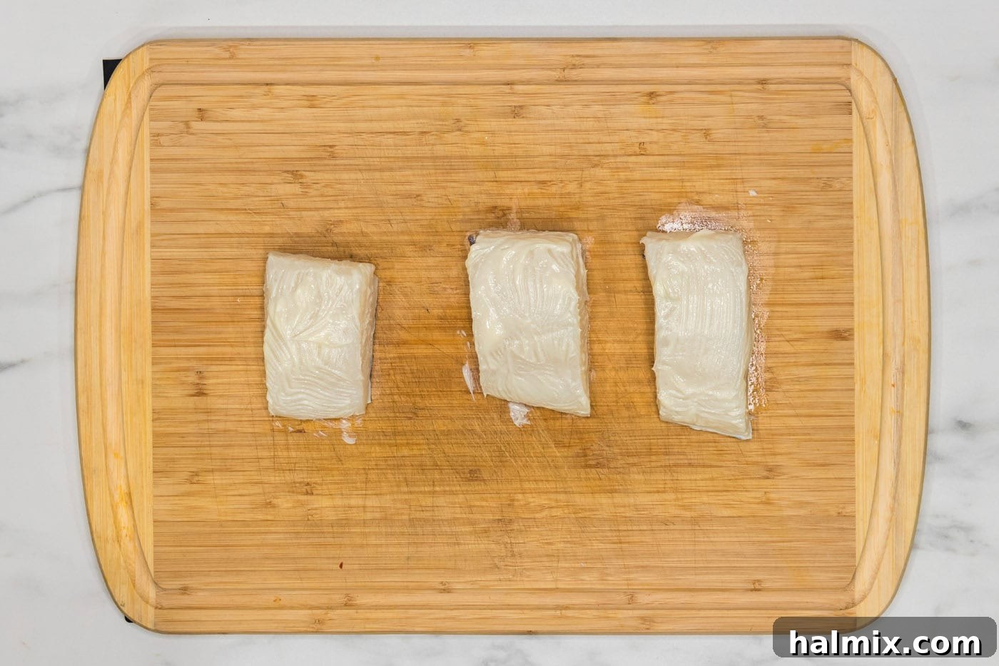 Golden Pan-Seared Chilean Sea Bass 6 chilean sea bass brushed with butter on a cutting board, ready for seasoning