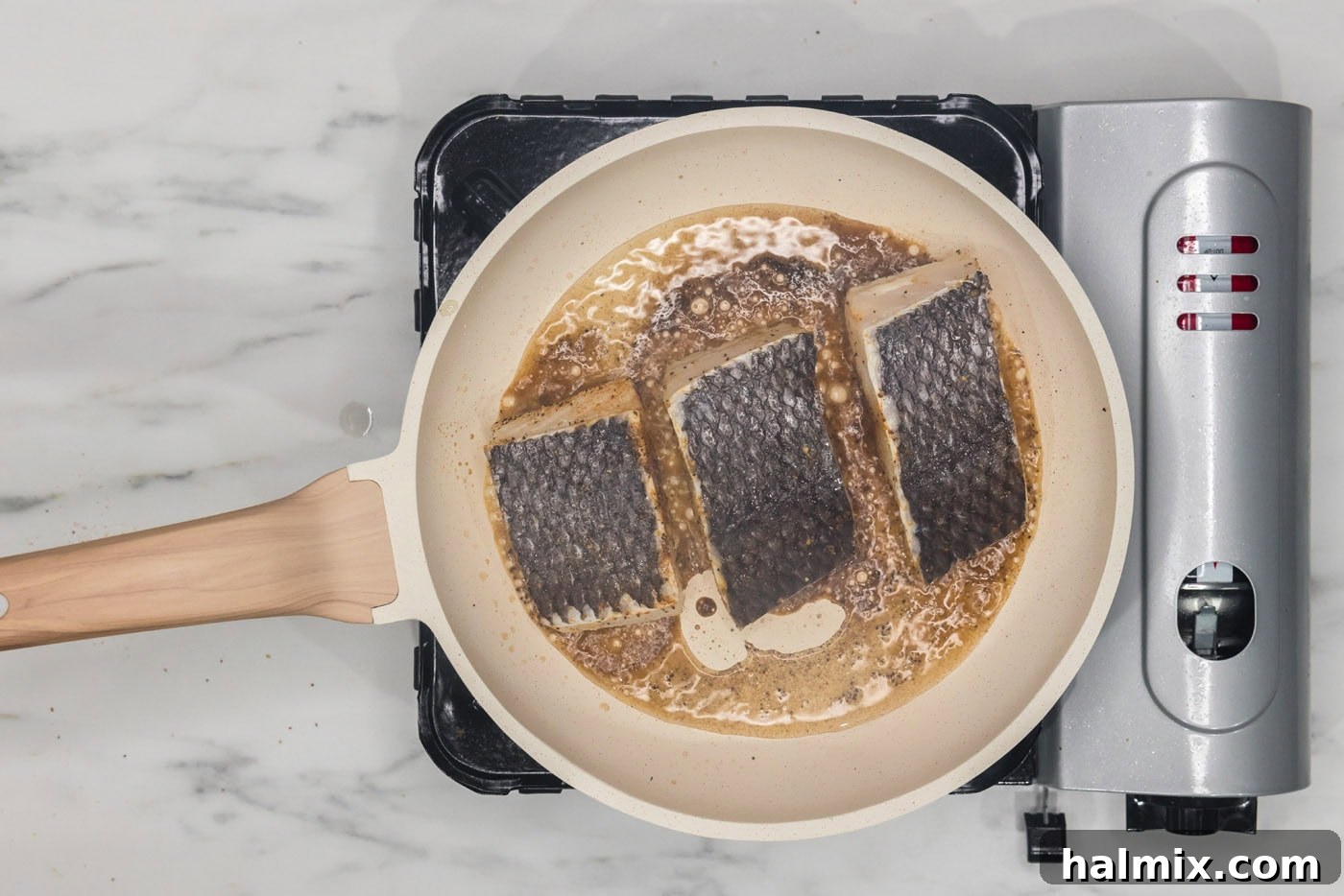 Golden Pan-Seared Chilean Sea Bass 8 chilean sea bass filets cooking in a skillet skin side up, steam visible