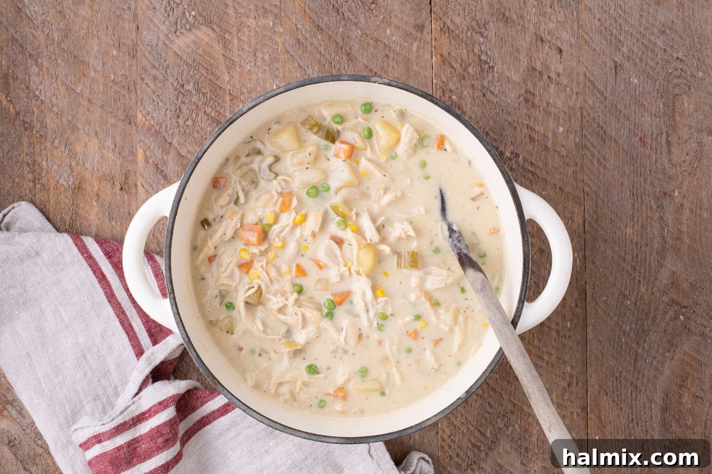 An overhead shot of a Dutch oven filled with freshly made chicken pot pie soup, ready to be served, with a ladle resting inside.