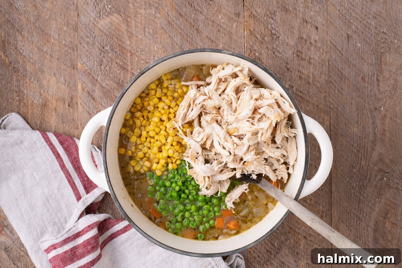 Shredded chicken, vibrant frozen peas, and golden frozen corn being added to the simmering soup in the Dutch oven.