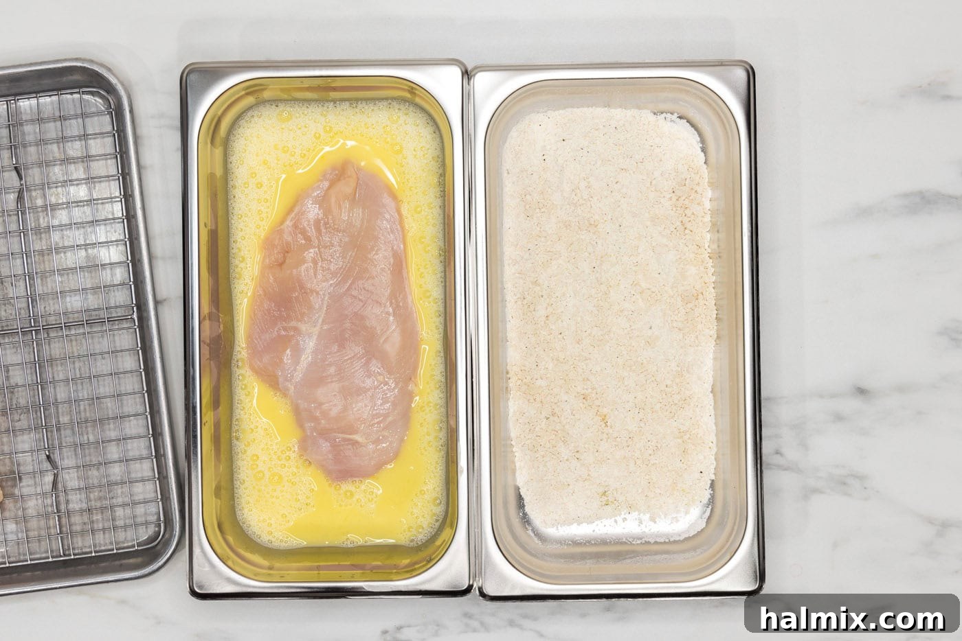 chicken breast in egg mixture inside a breading tray