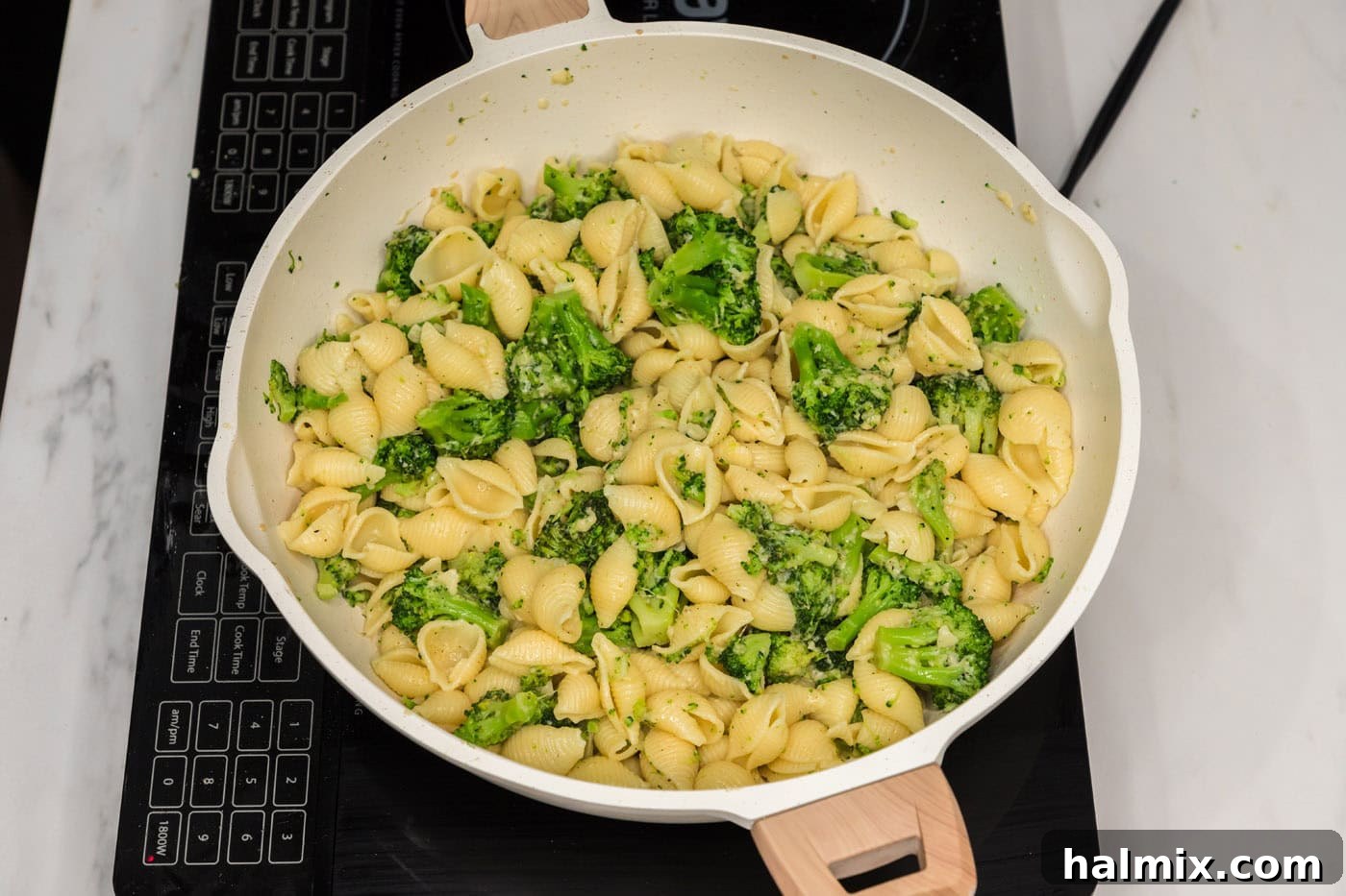 Broccoli pasta being tossed with parmesan cheese and reserved pasta water in a skillet to create the sauce.
