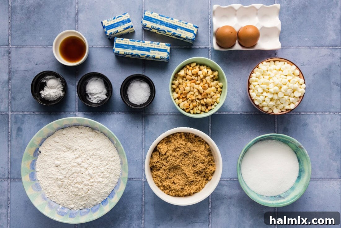 All the fresh ingredients laid out on a countertop, ready to be used for making White Chocolate Macadamia Nut Cookies, including butter, sugars, flour, eggs, white chocolate chips, and macadamia nuts.