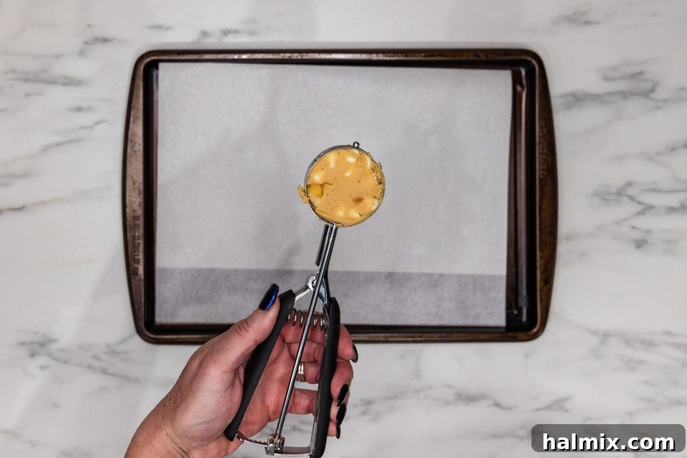 White chocolate macadamia nut cookie dough being scooped into a 3-tablespoon cookie scoop, ready for baking.