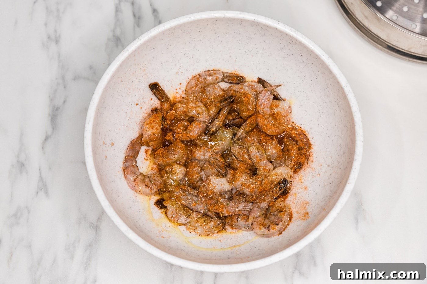 Raw shrimp in a bowl with Old Bay seasoning and olive oil, ready for tossing.