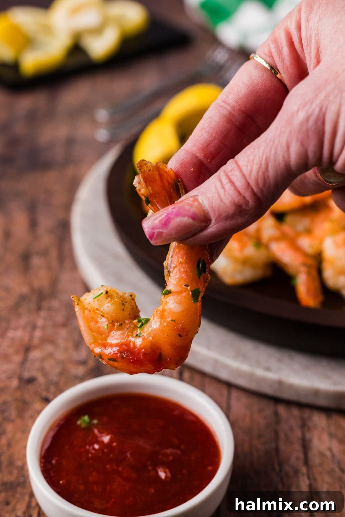Hand holding a perfectly Steamed Shrimp above a bowl of zesty cocktail sauce, ready for dipping.