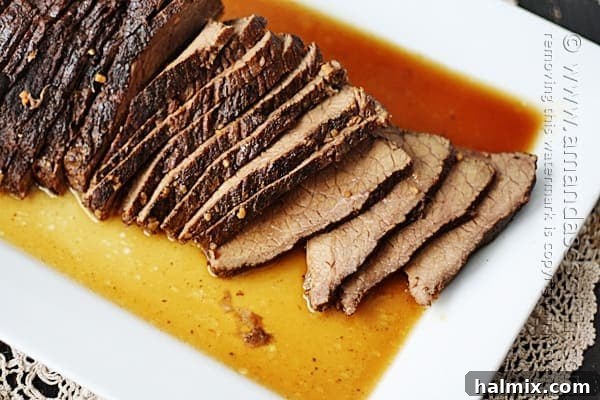 Sliced slow cooker beef roast with brandy sauce on a white platter, garnished with fresh herbs.