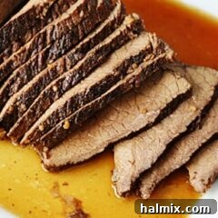 A close up of sliced slow cooker roast with brandy sauce on a white platter.