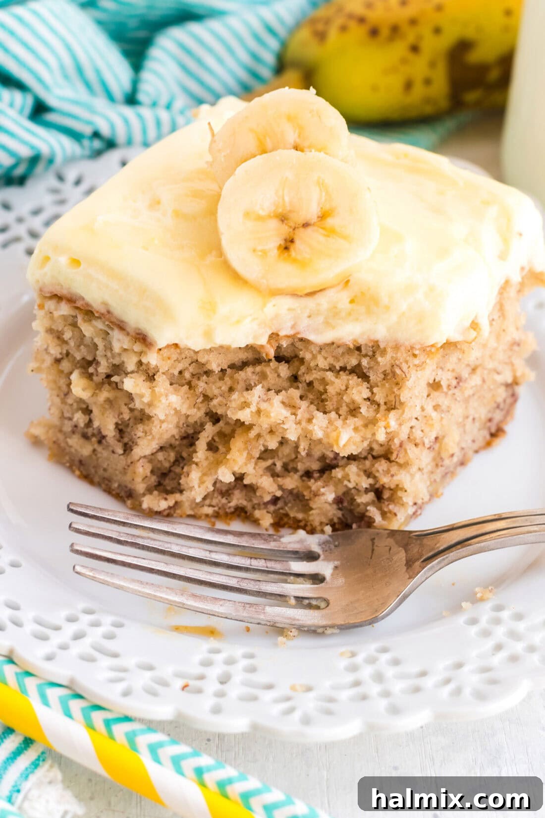 This easy banana cake using a cake mix is incredibly delicious, simple to make, and features a heavenly banana-flavored whipped cream frosting! A delectable slice of banana cake with a bite taken out, showcasing the moist interior and fluffy banana whipped cream frosting.