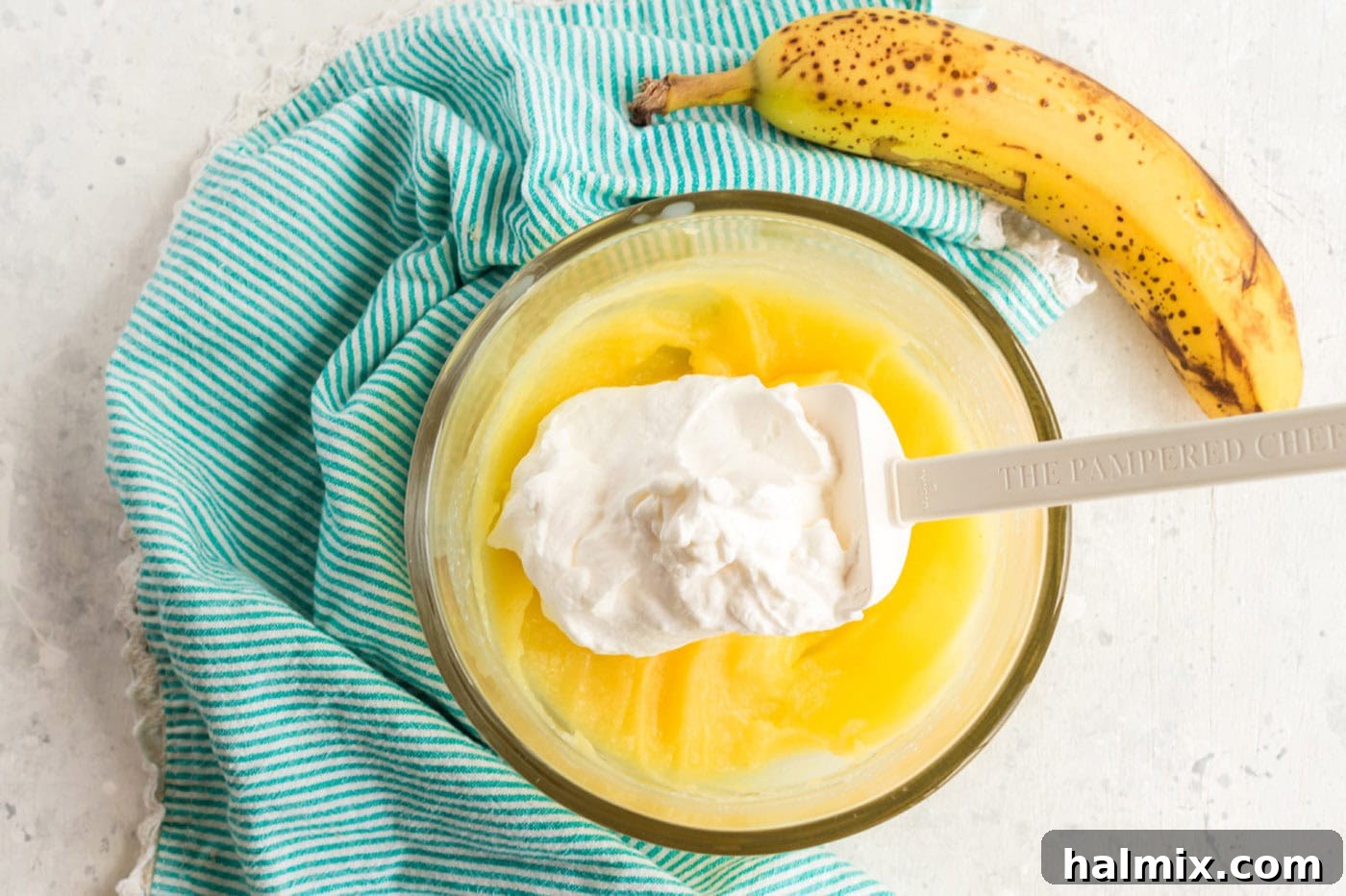 Simply Delicious Banana Cake 9 Fluffy whipped cream being gently folded into the prepared banana pudding mixture in a bowl.