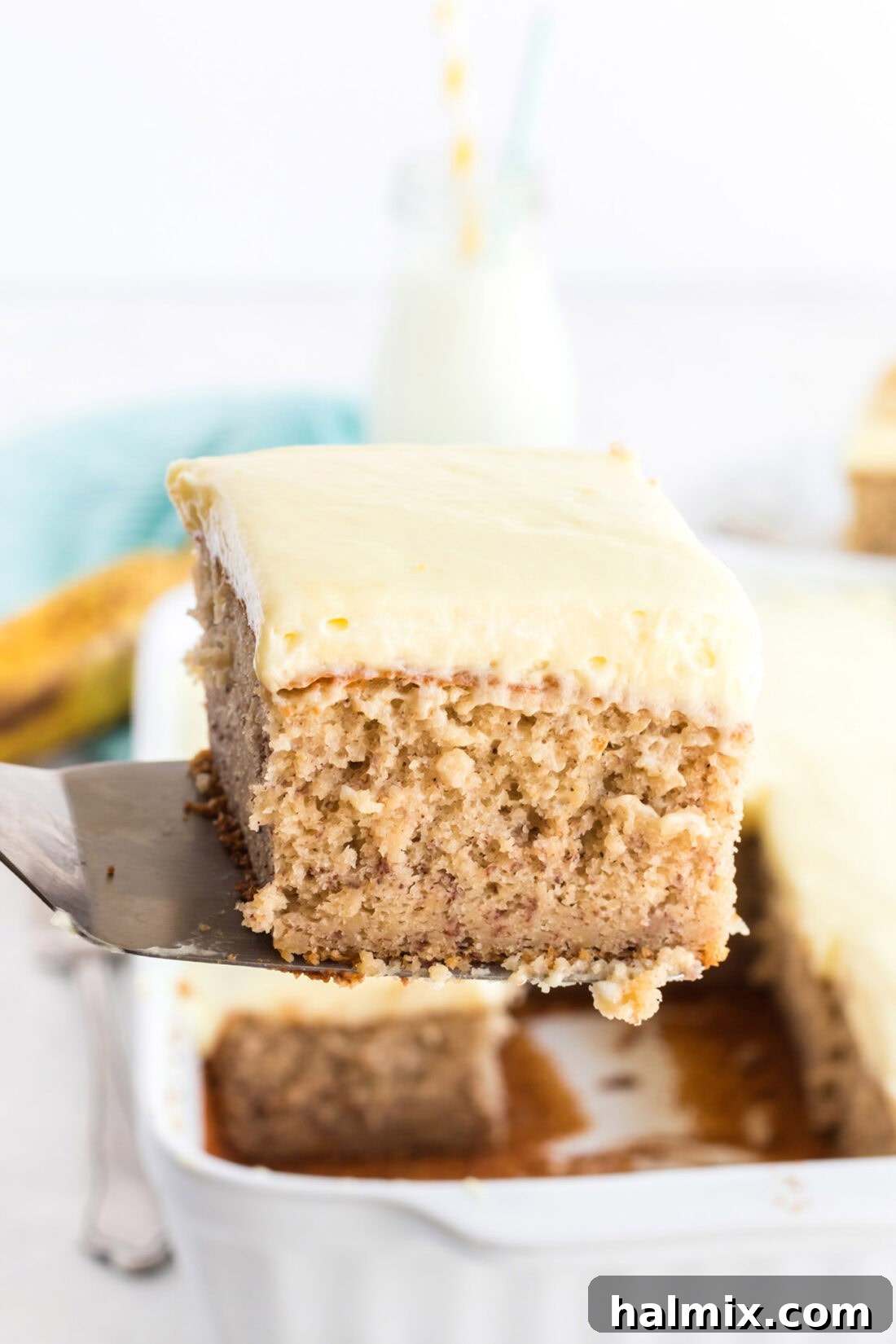 This easy banana cake using cake mix is positively delicious, simple to prepare, and features a fantastic banana whipped cream frosting! A spatula delicately holding a slice of moist banana cake topped with whipped cream frosting, ready to be served.