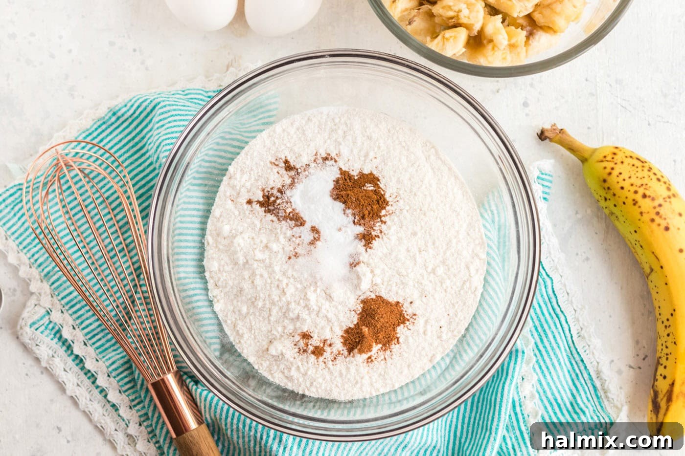 A bowl containing white cake mix with added spices like cinnamon, nutmeg, baking soda, and salt, ready for whisking.