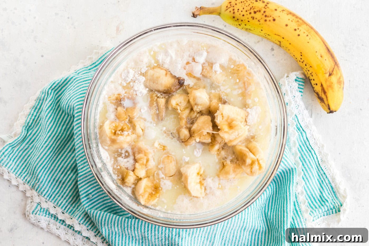 Mashed bananas added to a bowl containing other wet and dry cake ingredients, ready for mixing into batter.