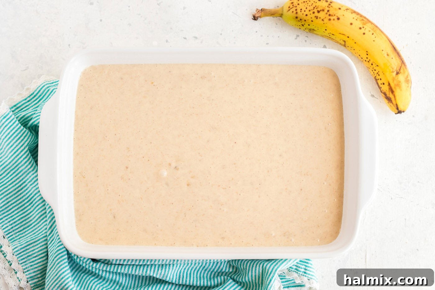 Banana cake batter evenly spread in a 13x9 inch baking pan, ready to be placed in the oven for baking.