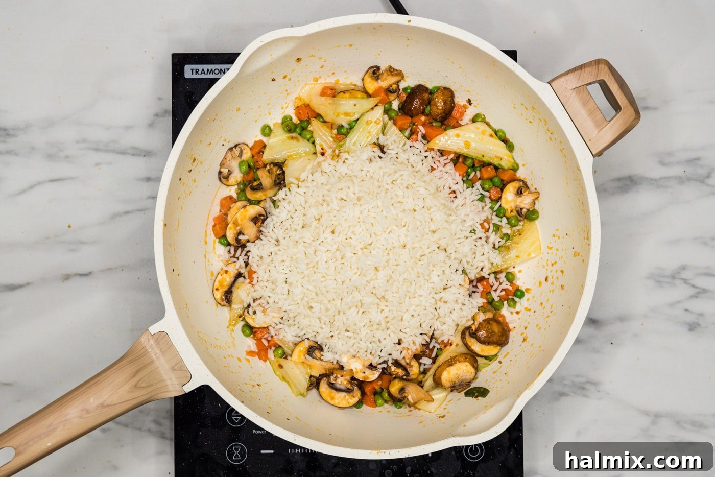 Cooked rice being added to a skillet with stir-fried vegetables