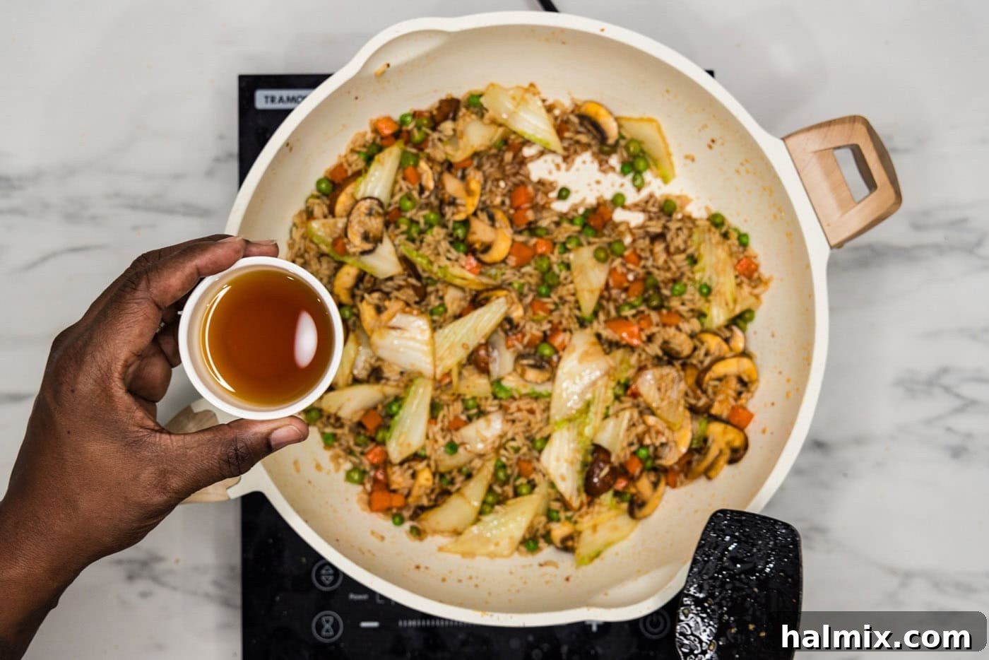 Adding sesame oil to the Korean fried rice in a skillet for final flavoring