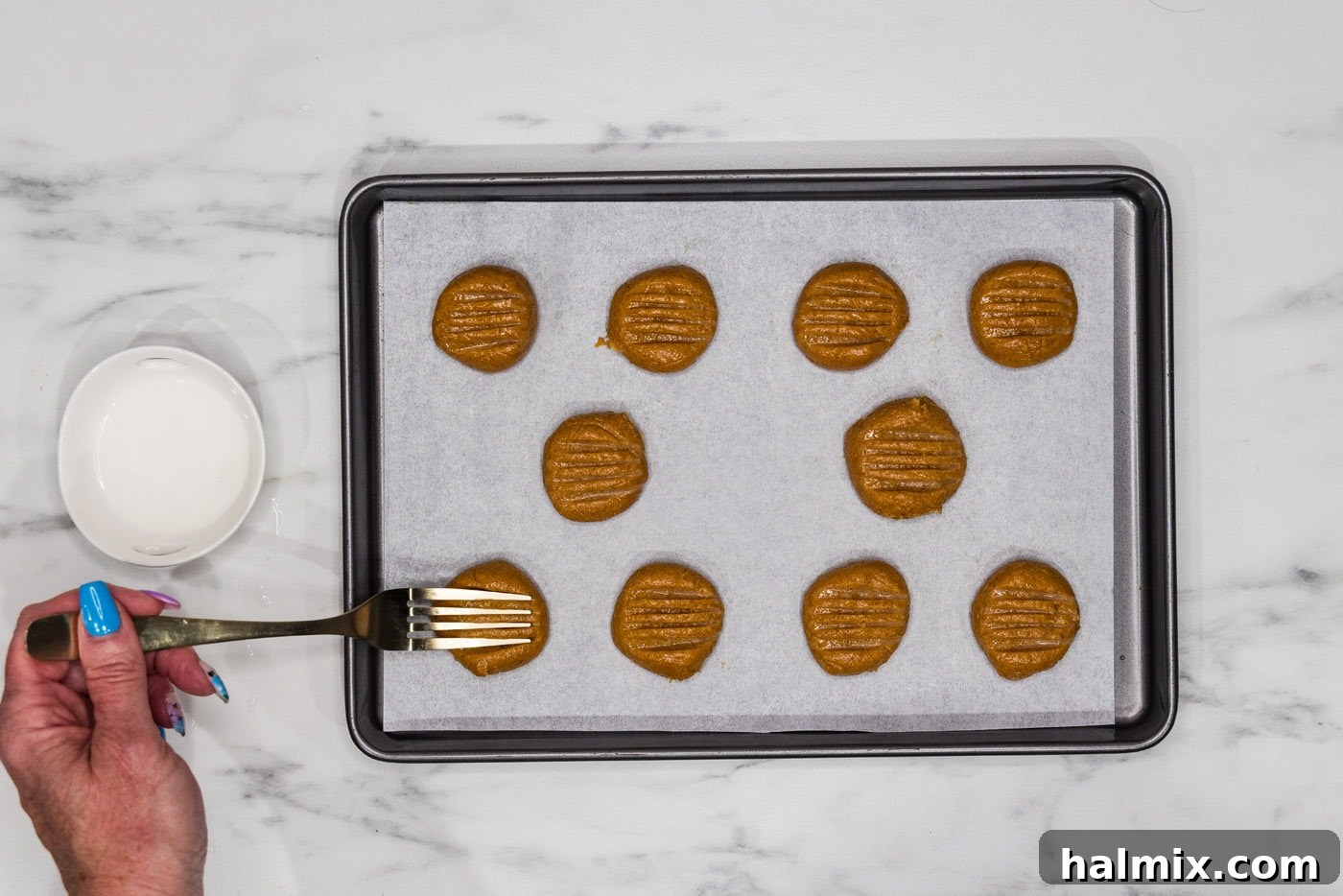 fork pressing into peanut butter cookie dough on a baking sheet, creating a crisscross pattern
