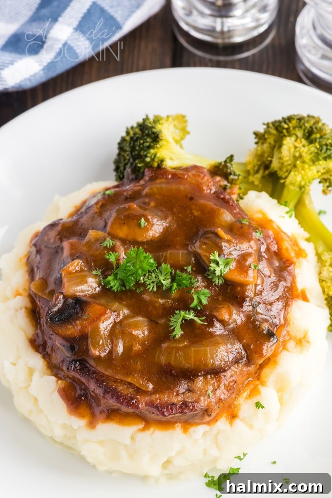 Oven swiss steak generously covered in gravy, served on a bed of creamy mashed potatoes
