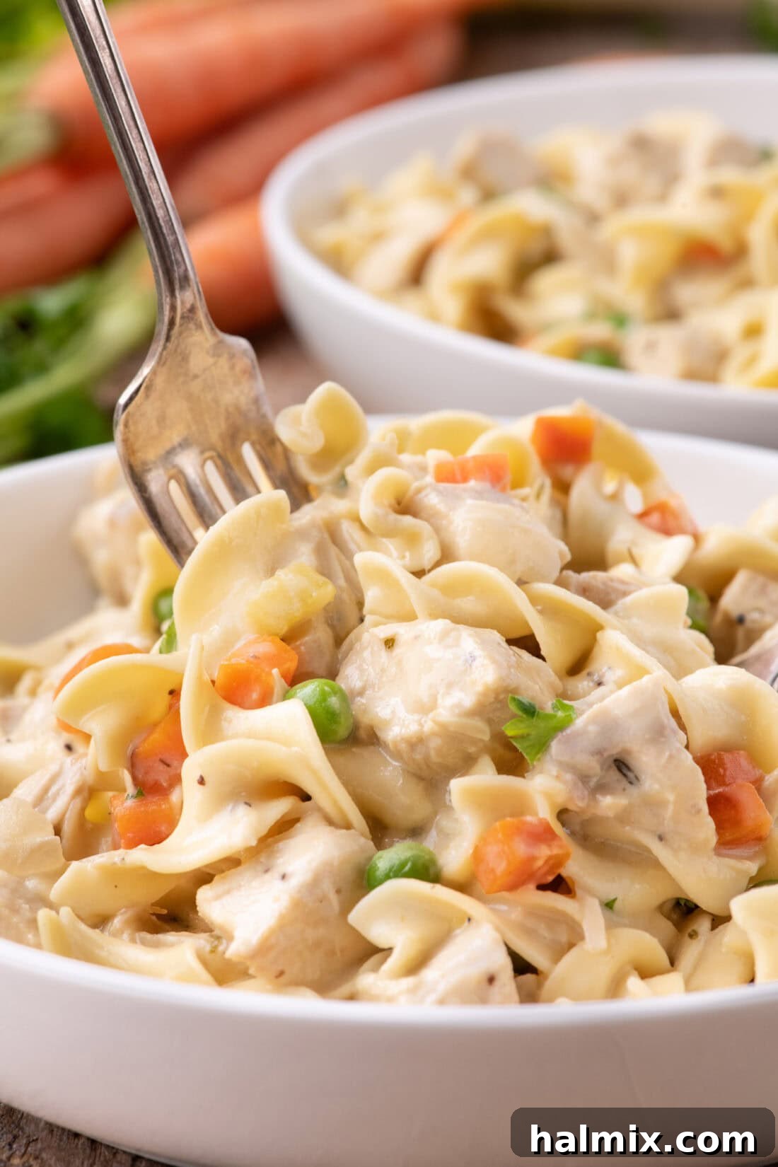 Creamy Chicken Pot Pie Pasta 5 A close-up of a fork digging into a bowl of creamy Chicken Pot Pie Pasta, highlighting the noodles and chicken pieces.