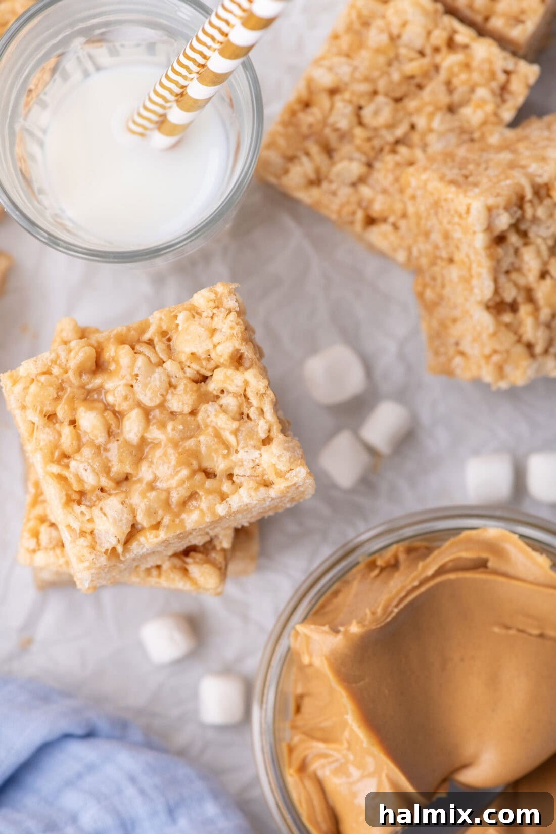Peanut Butter Crunch Bars 11 Stacked Peanut Butter Rice Krispie Treats beautifully arranged, with a small bowl of creamy peanut butter and a glass of refreshing milk on the side, inviting a delightful snack time.
