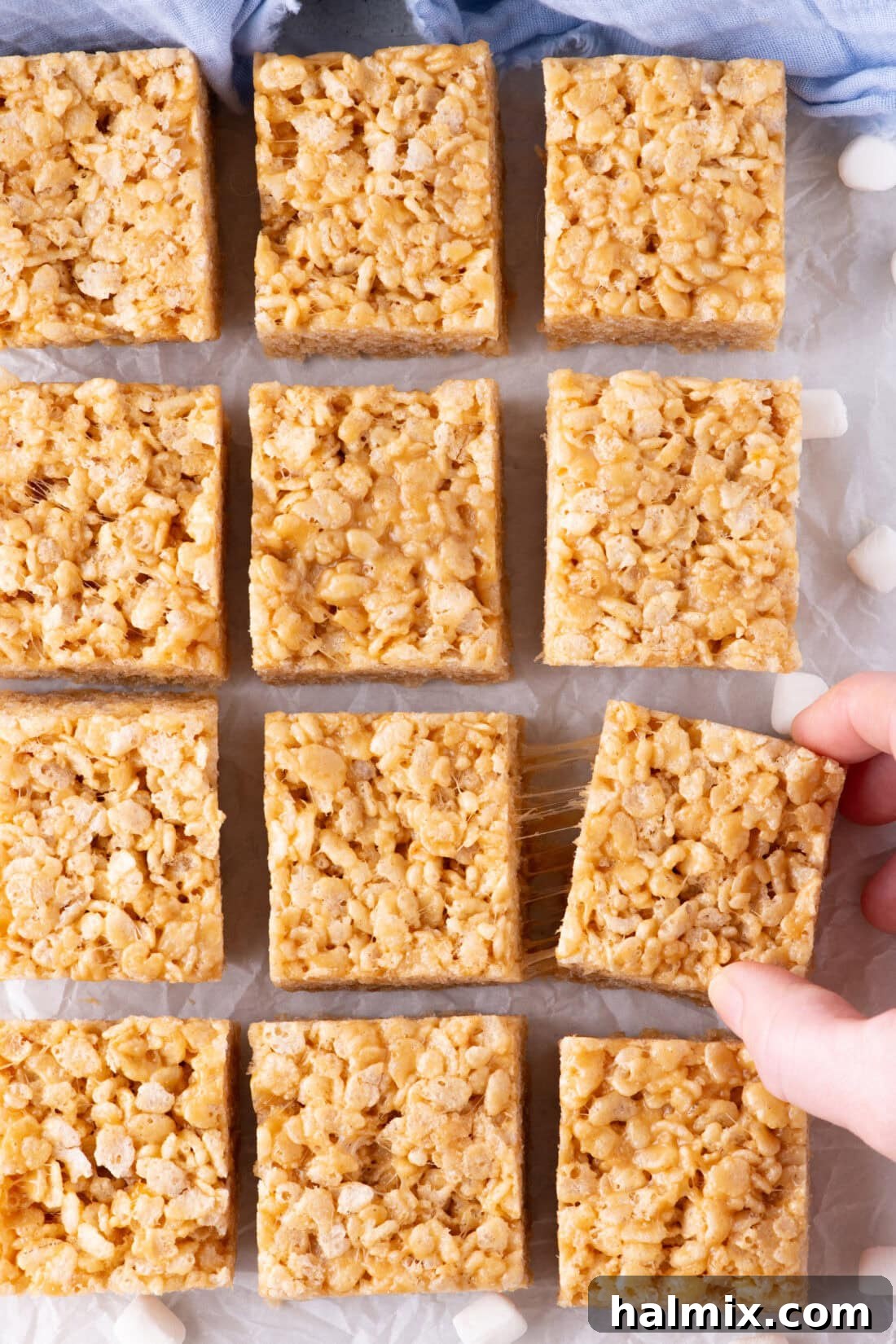Peanut Butter Crunch Bars 3 Freshly cut Peanut Butter Rice Krispie Treats arranged neatly on parchment paper, showcasing their perfect square shape and appealing golden color.