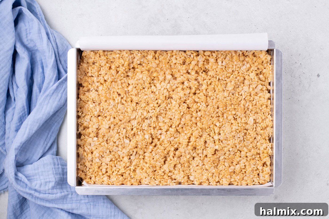 Peanut Butter Crunch Bars 9 The peanut butter Rice Krispies mixture evenly pressed into a baking pan lined with parchment paper, appearing smooth and ready to cool.