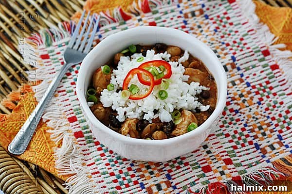 A close up of a white bowl filled with three bean salsa chicken and rice, showcasing the colorful ingredients, tender chicken, and rich sauce.