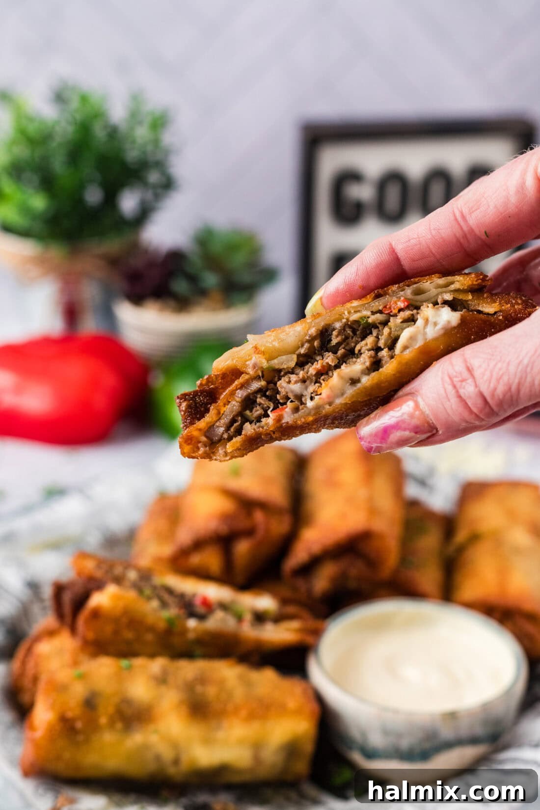 Hand holding up a Philly Cheesesteak Egg Roll cut in half