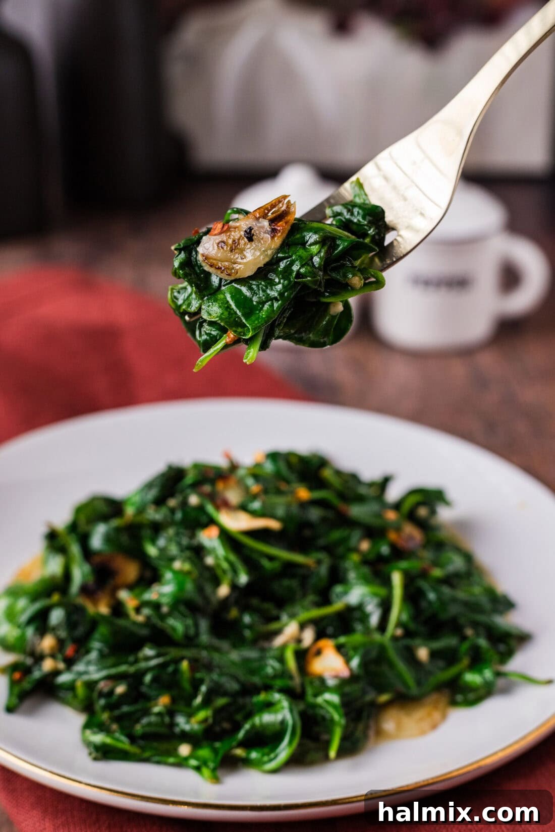 Fork of Stir Fried Spinach held above a plate of Stir Fried Spinach