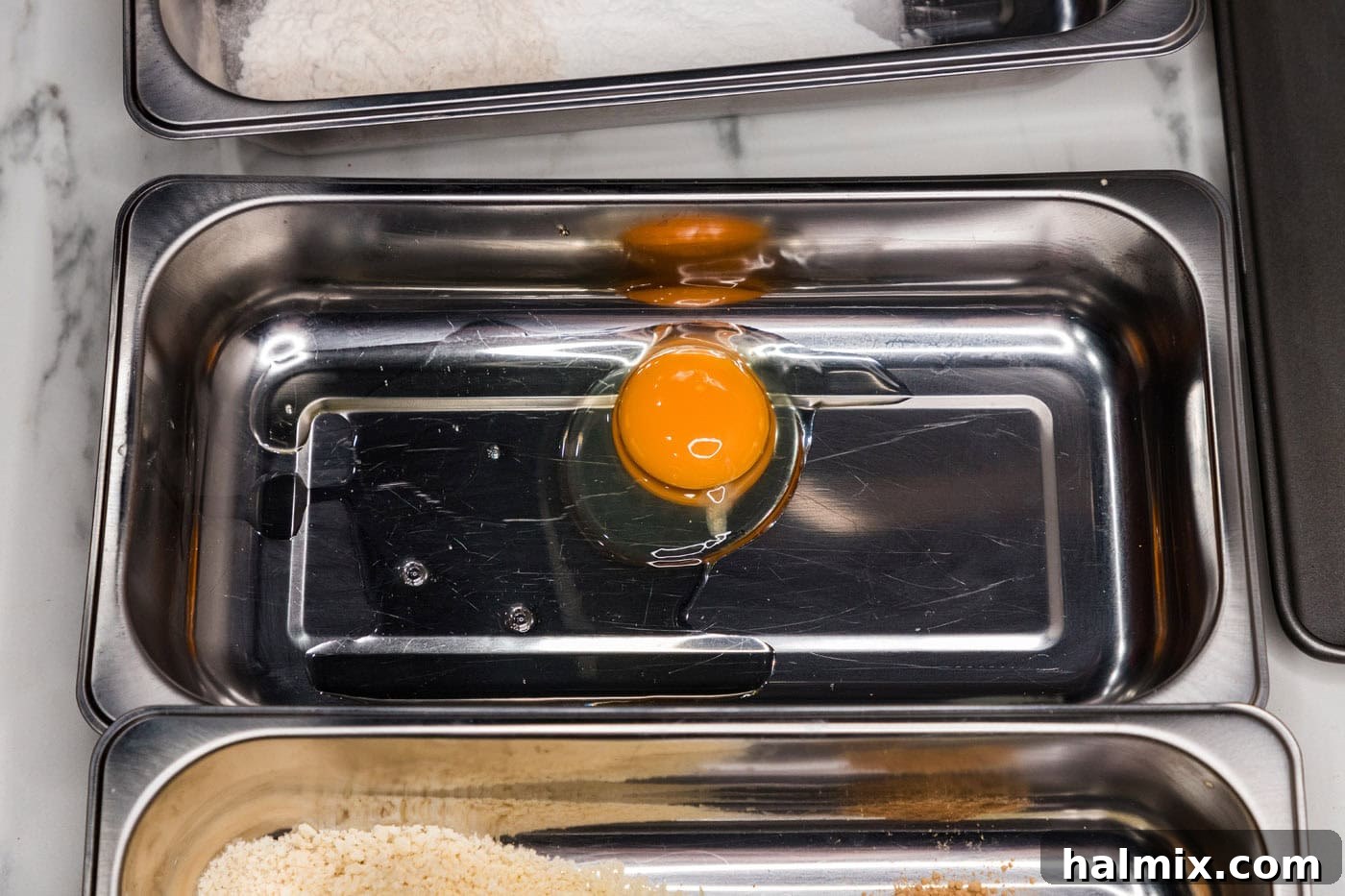A shallow breading tray containing a whisked egg and water mixture for the egg wash.