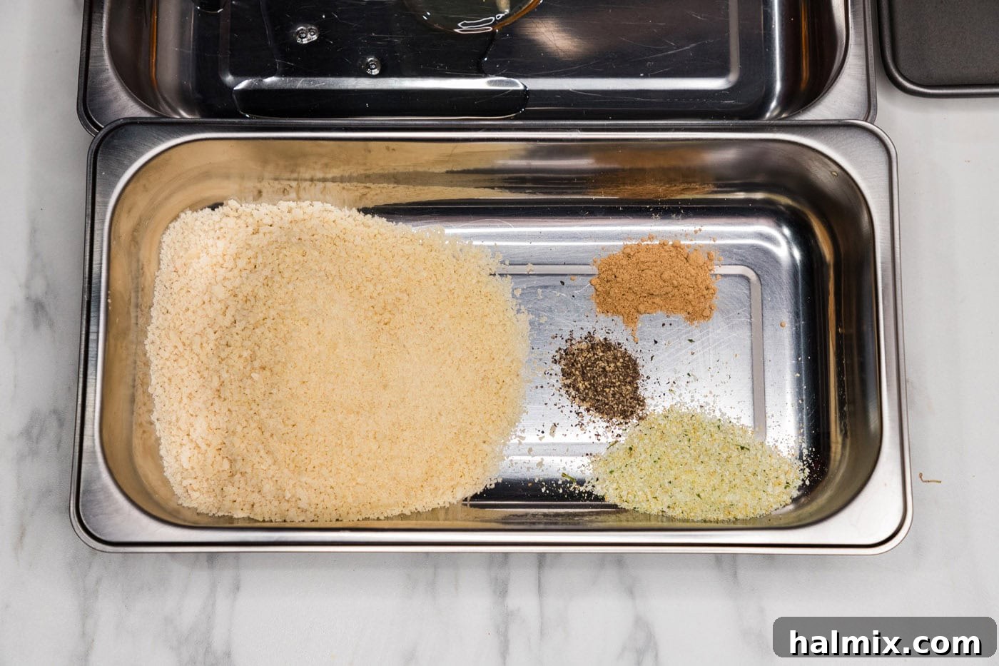 A shallow breading tray with panko breadcrumbs seasoned with garlic salt, pepper, and ginger.