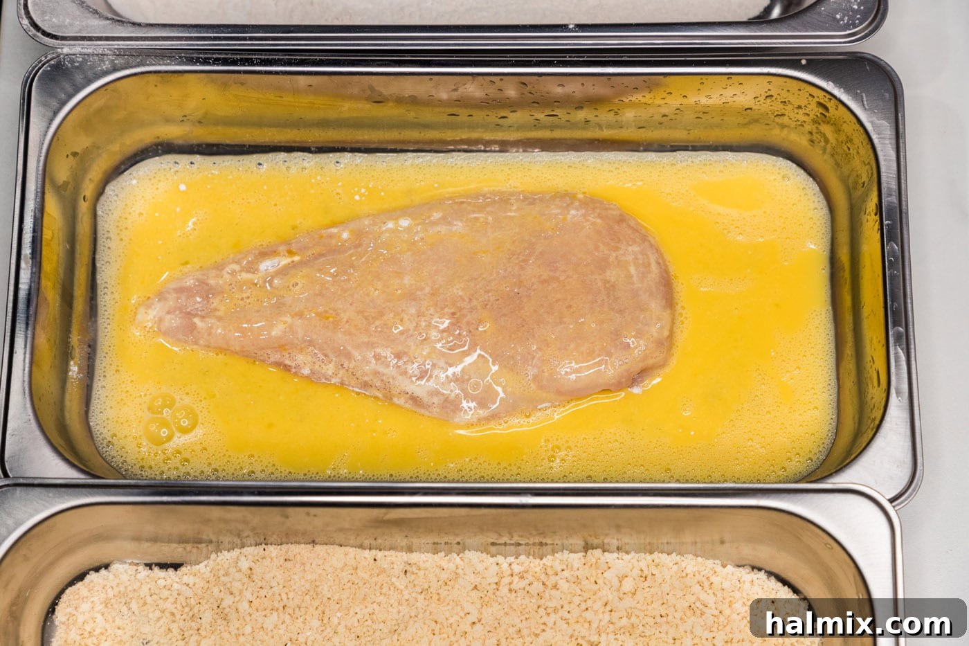 A chicken breast being dredged through the egg wash.