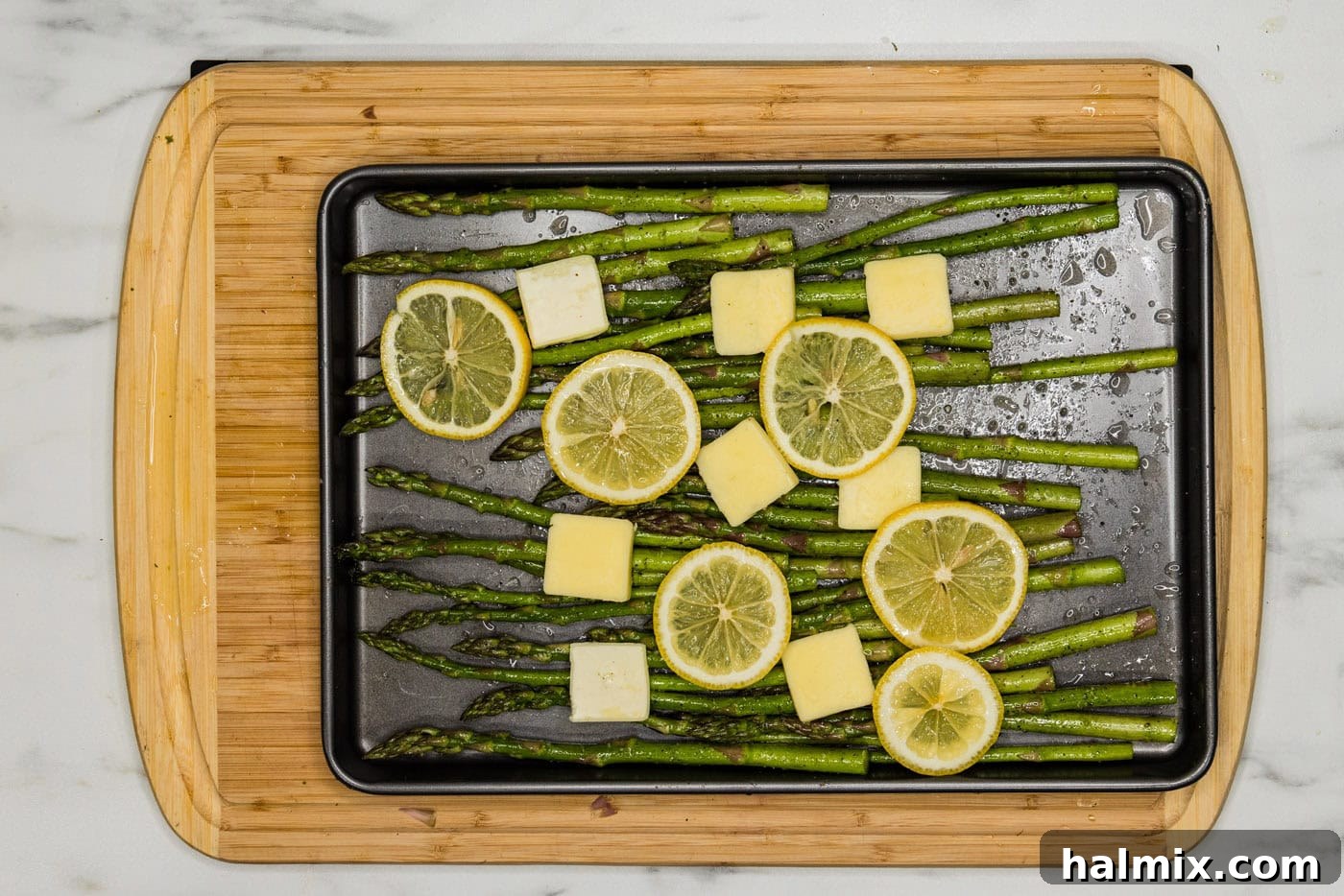Bright Lemon Asparagus 8 asparagus on a baking pan with butter pats and lemon slices arranged on top
