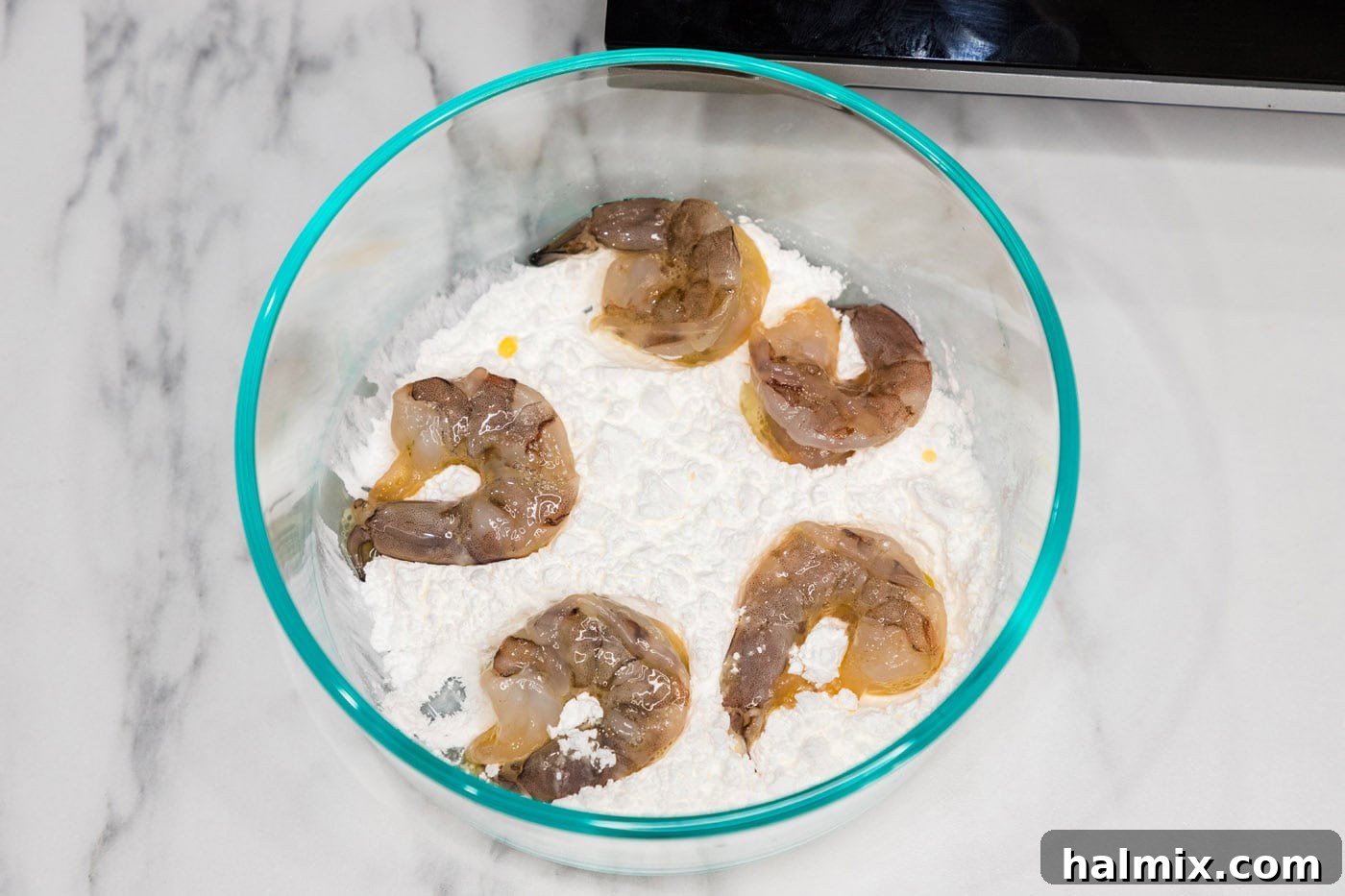 Shrimp being dredged in flour in a bowl.