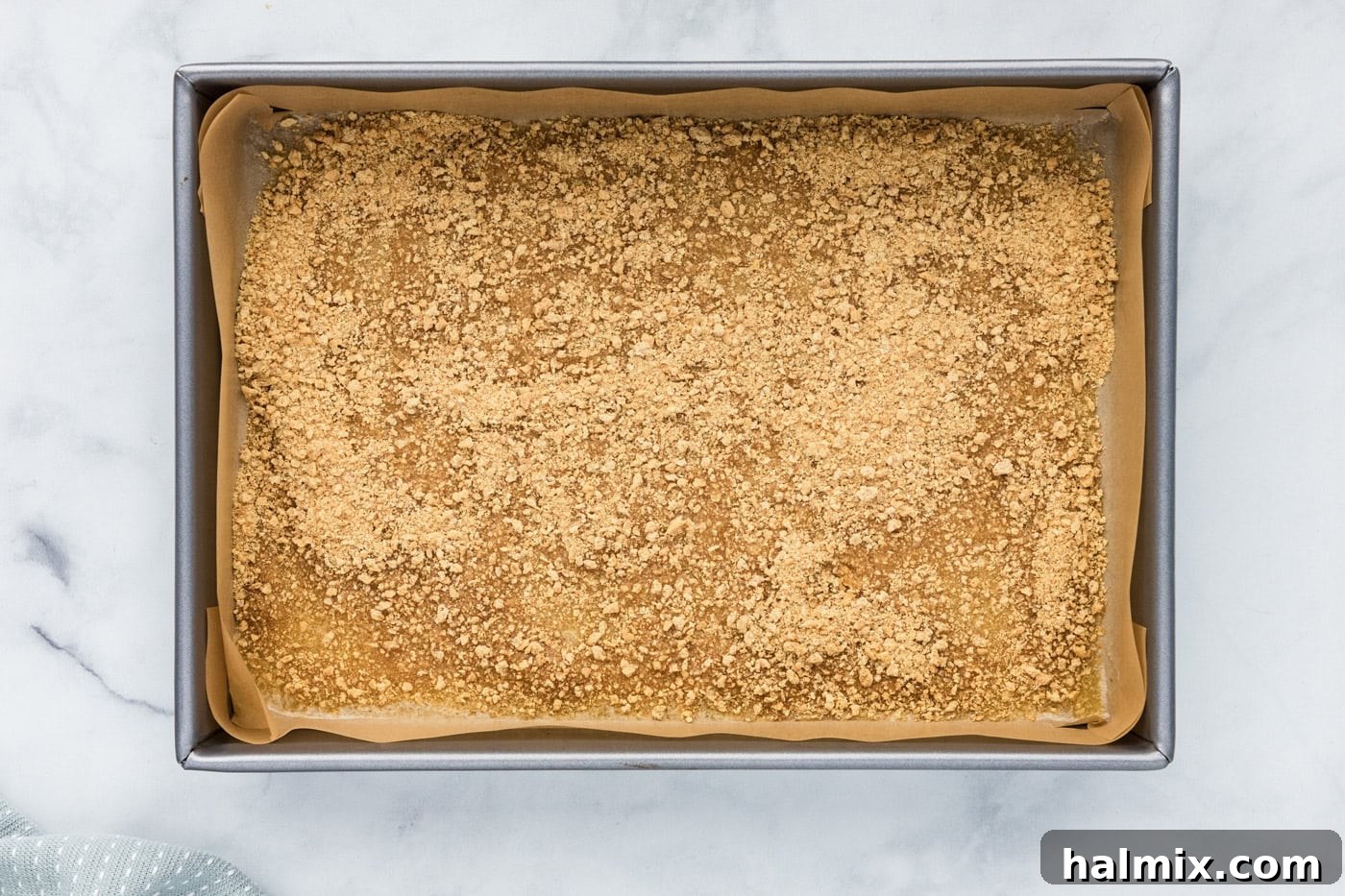 Graham cracker crumbs sprinkled over melted butter in a baking pan.