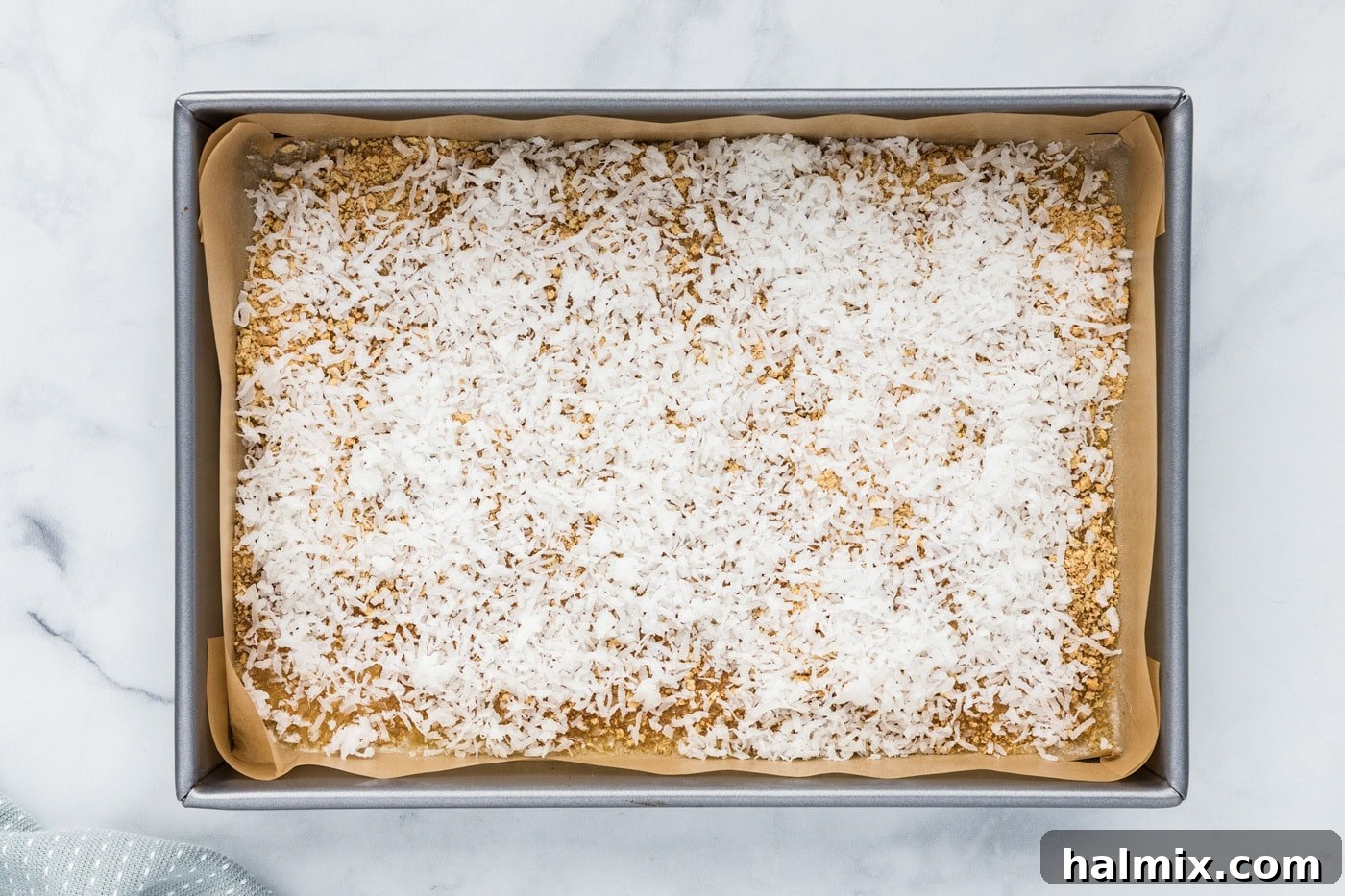 Shredded coconut sprinkled over graham crumbs and melted butter in a baking pan.