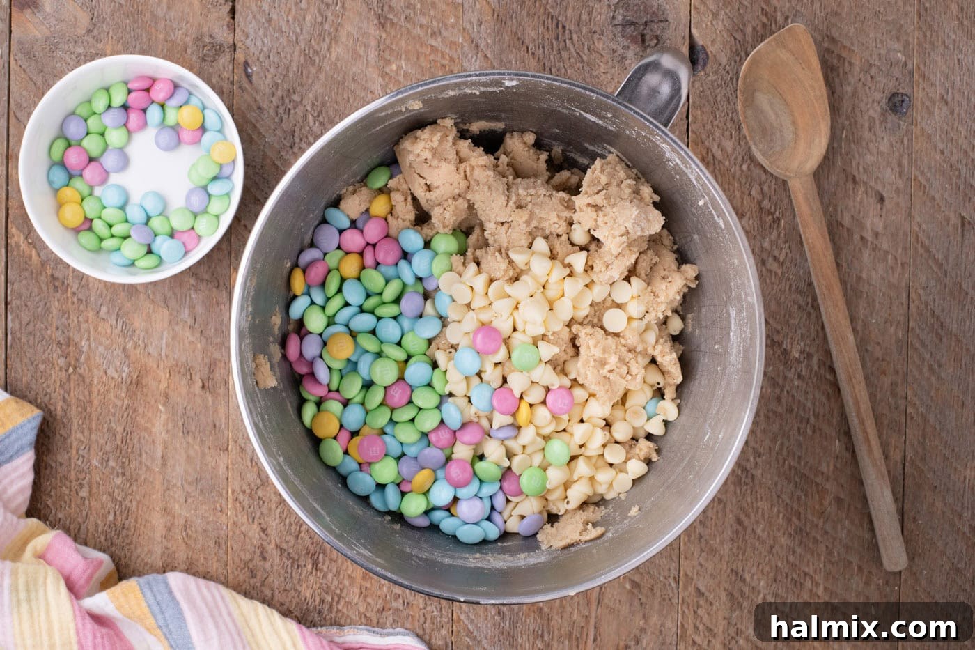 White chocolate chips and Easter M&M's being folded into the cookie dough in a mixing bowl.