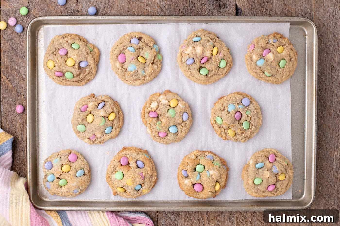 Overhead view of freshly baked Easter M&M cookies on a baking sheet, with extra chocolate chips and M&Ms pressed into their tops.