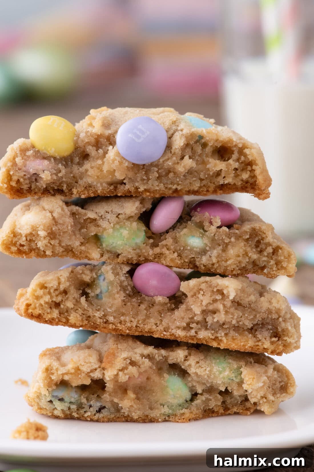 Stack of freshly baked Easter M&M Cookies, showing a cookie broken in half to reveal its soft, chewy interior with melted white chocolate and colorful M&Ms.