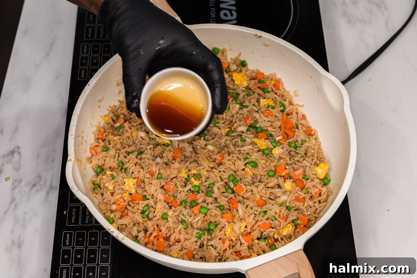 Pouring toasted sesame oil into vegetable fried rice for an aromatic finish