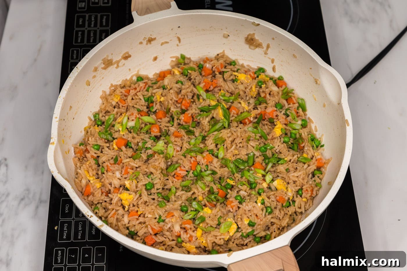 Sliced green onions on top of vegetable fried rice in a skillet, ready to serve