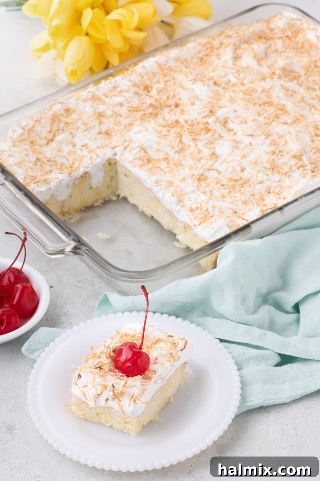 Slice of Coconut Poke Cake on a plate with the rest of the cake in the background