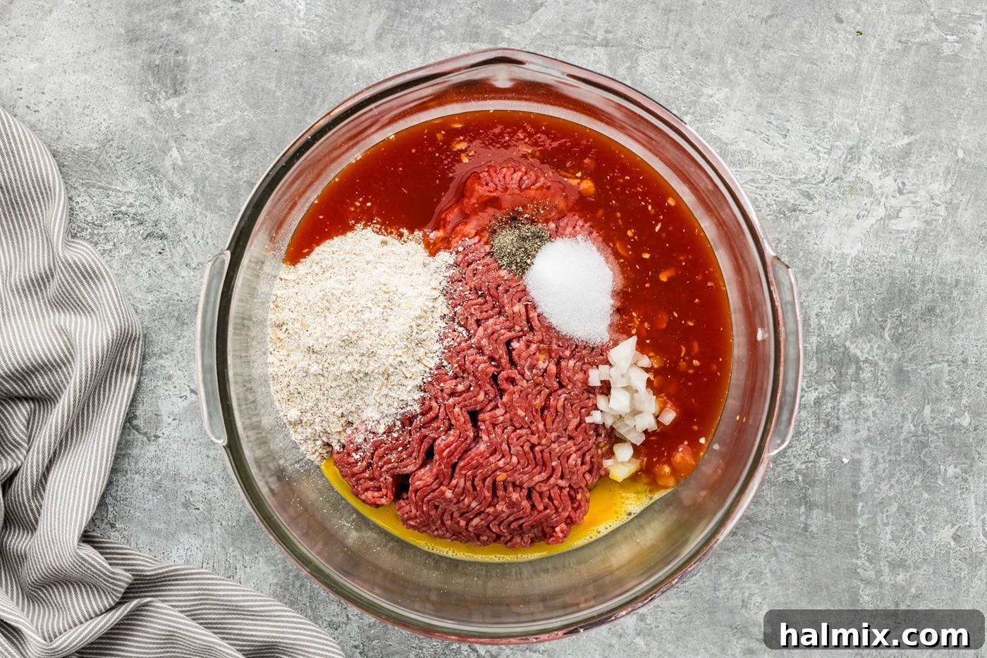 A bowl filled with raw meatloaf ingredients, including ground beef, oats, and seasonings, ready for mixing.