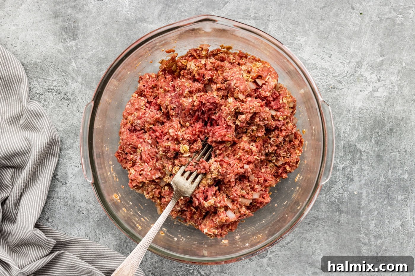A fork resting in a bowl of combined meatloaf ingredients, showing the texture before pressing into a pan.