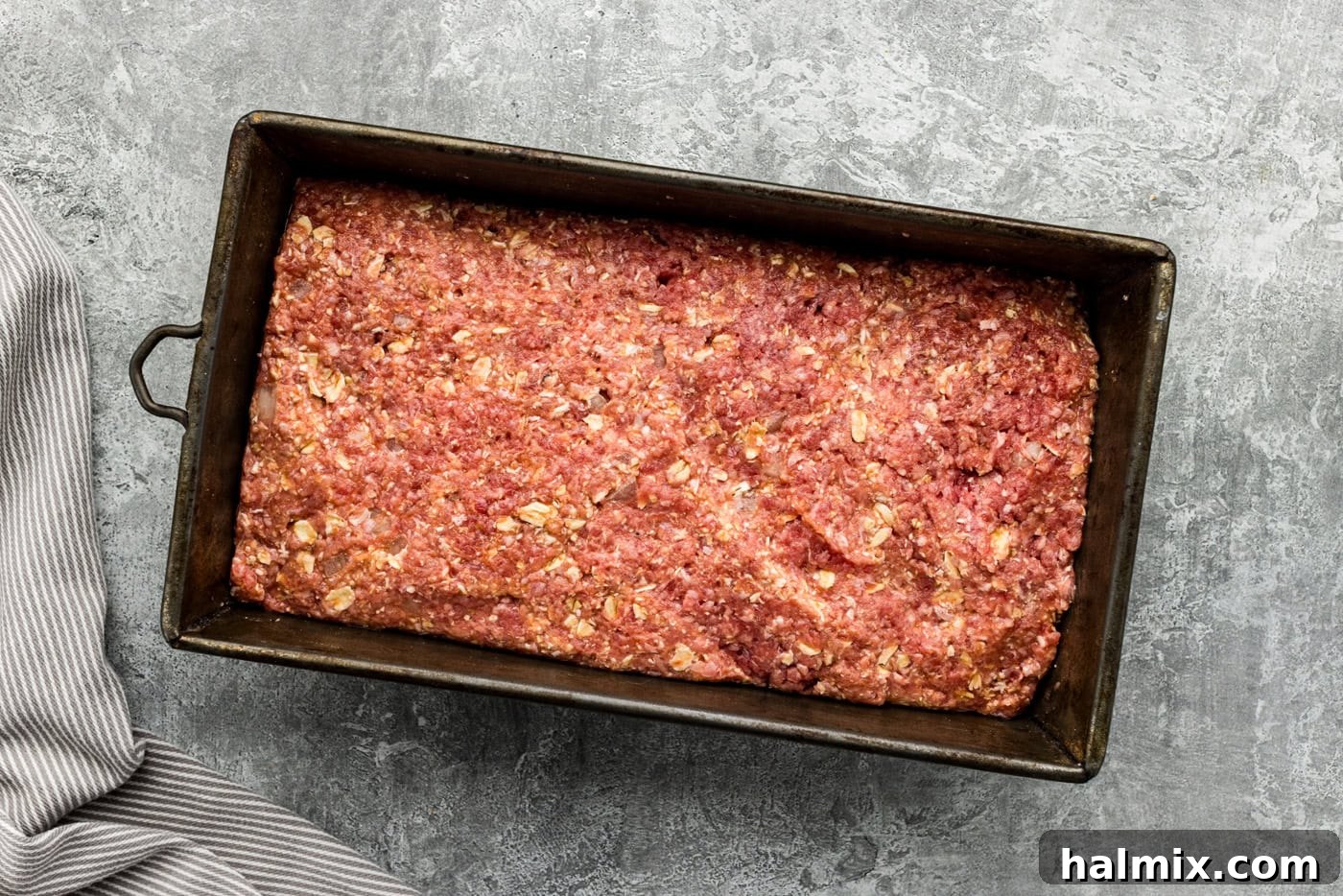 Raw meatloaf mixture firmly pressed into an ungreased loaf pan, ready for the oven.