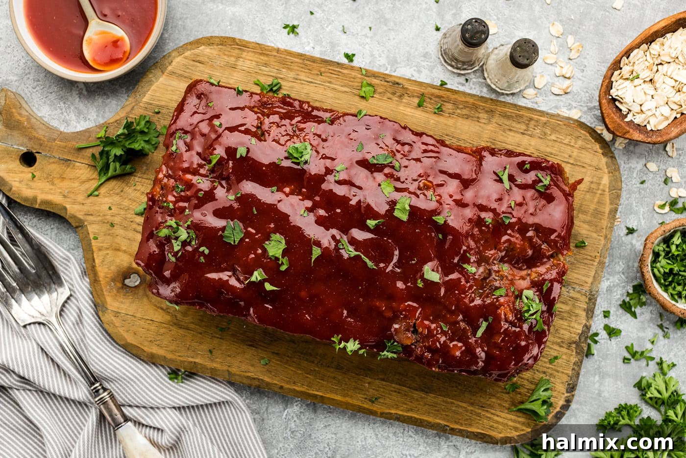 An overhead photo of a beautifully glazed and cooked Quaker Oats meatloaf on a cutting board, garnished with fresh chopped parsley.