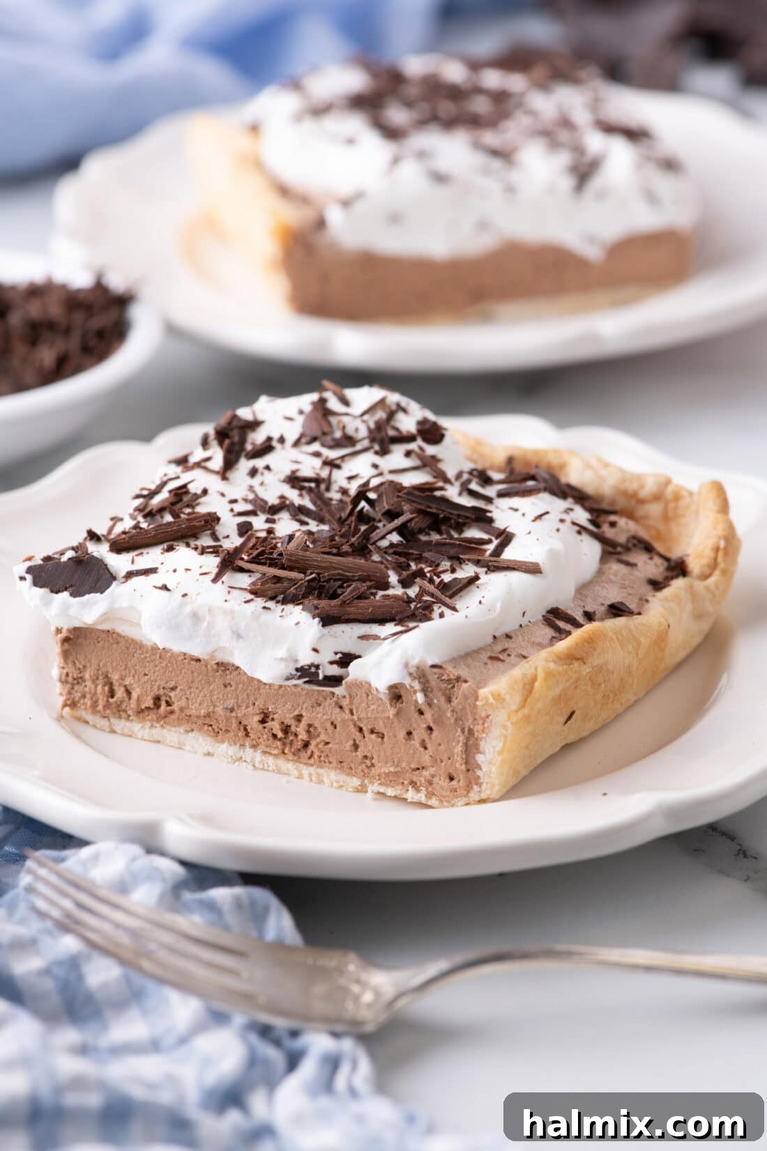 A perfect slice of French Silk Slab Pie on a white plate, showcasing the chocolate filling and whipped cream topping with chocolate shavings.