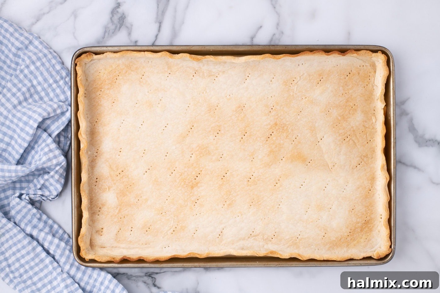 A perfectly baked, golden-brown pie crust resting in a jelly roll pan, cooled and ready for filling.